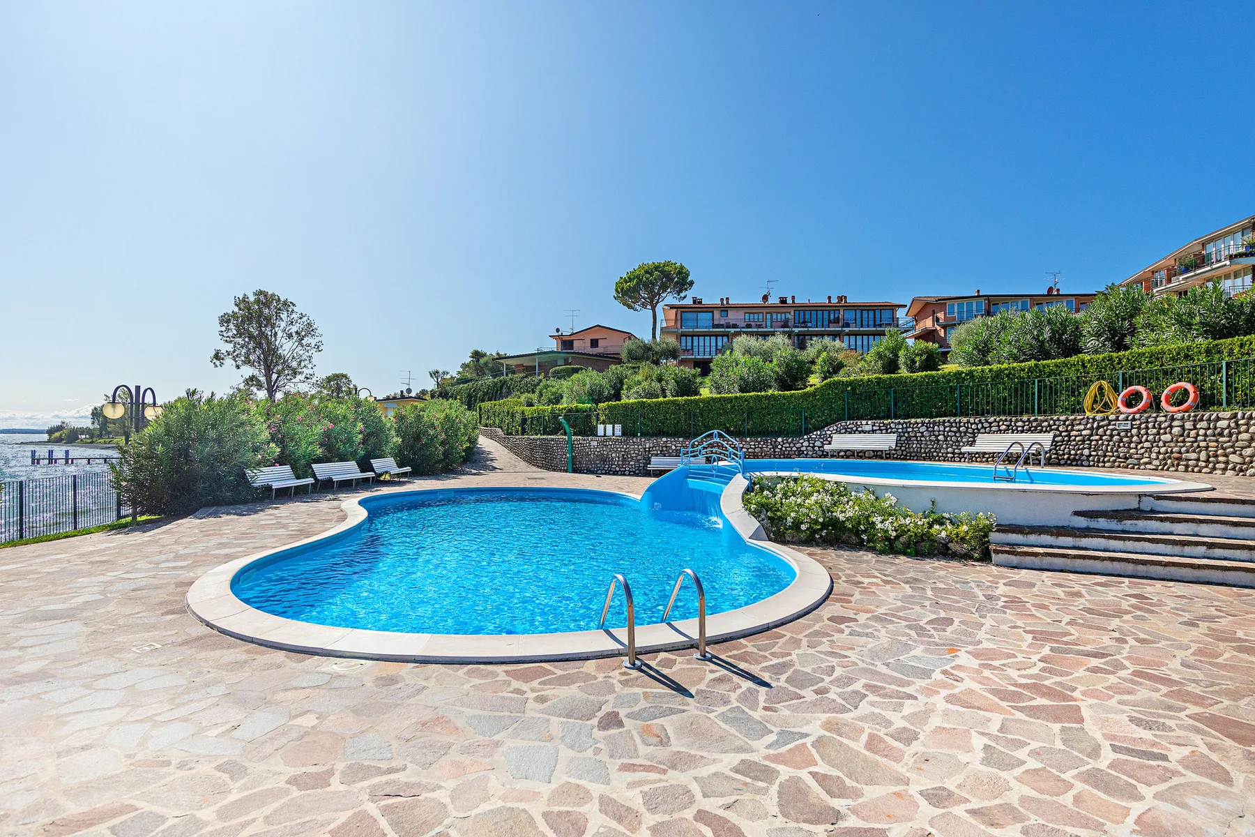 An outdoor swimming pool sits beside a stone-paved terrace and landscaped greenery.