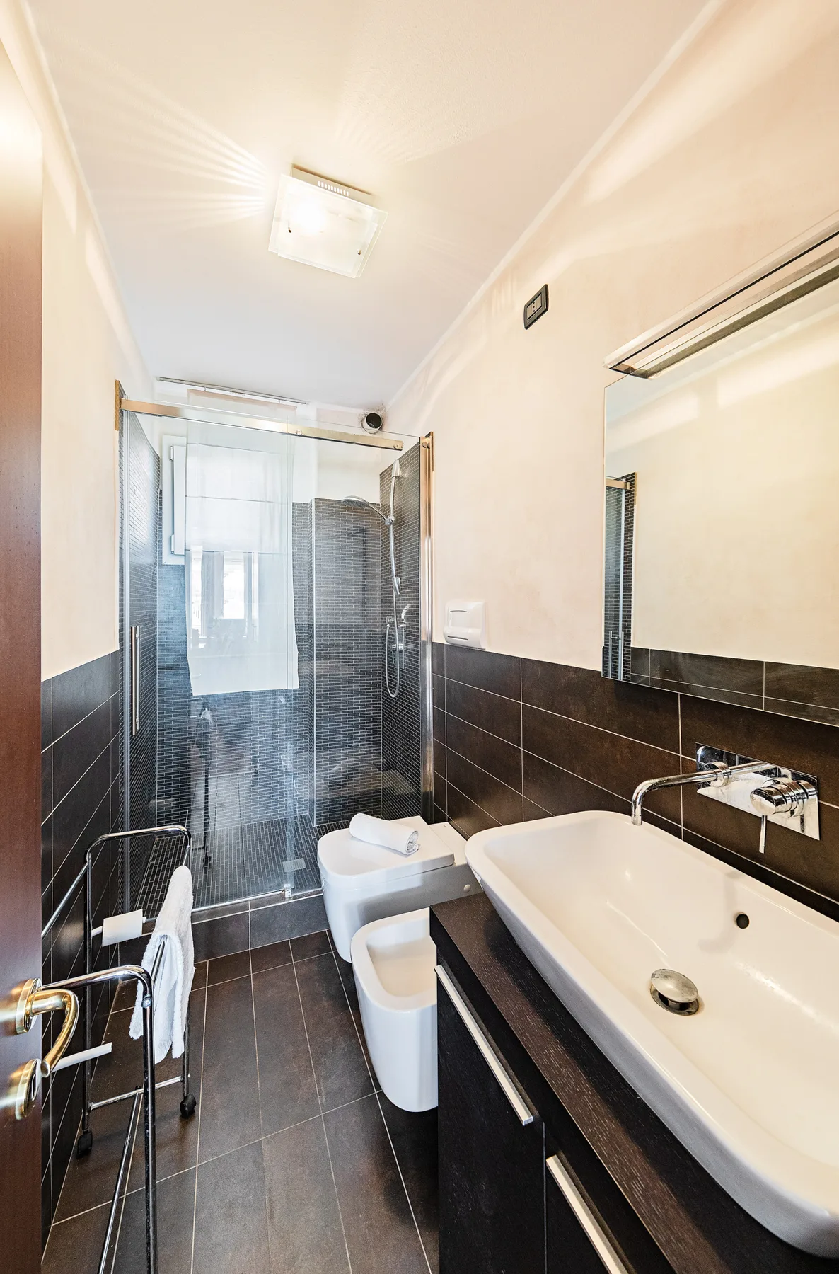 A narrow bathroom with a glass shower, toilet, and sink.