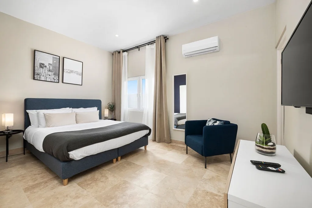 Unwind in your modern bedroom with plush bedding, a cozy armchair, and climate control—everything you need for restful nights and lazy mornings.