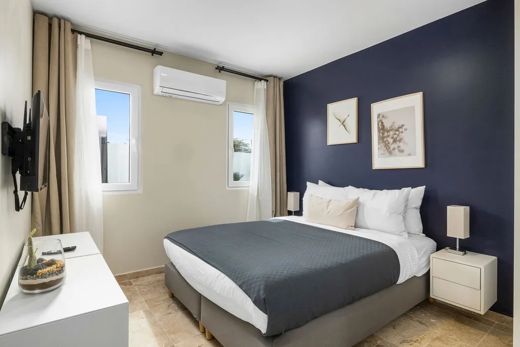 You'll rest easy in this calm bedroom with its plush bed, cooling AC, and natural light streaming through the windows. The deep navy accent wall adds a modern, cozy touch to your personal retreat.