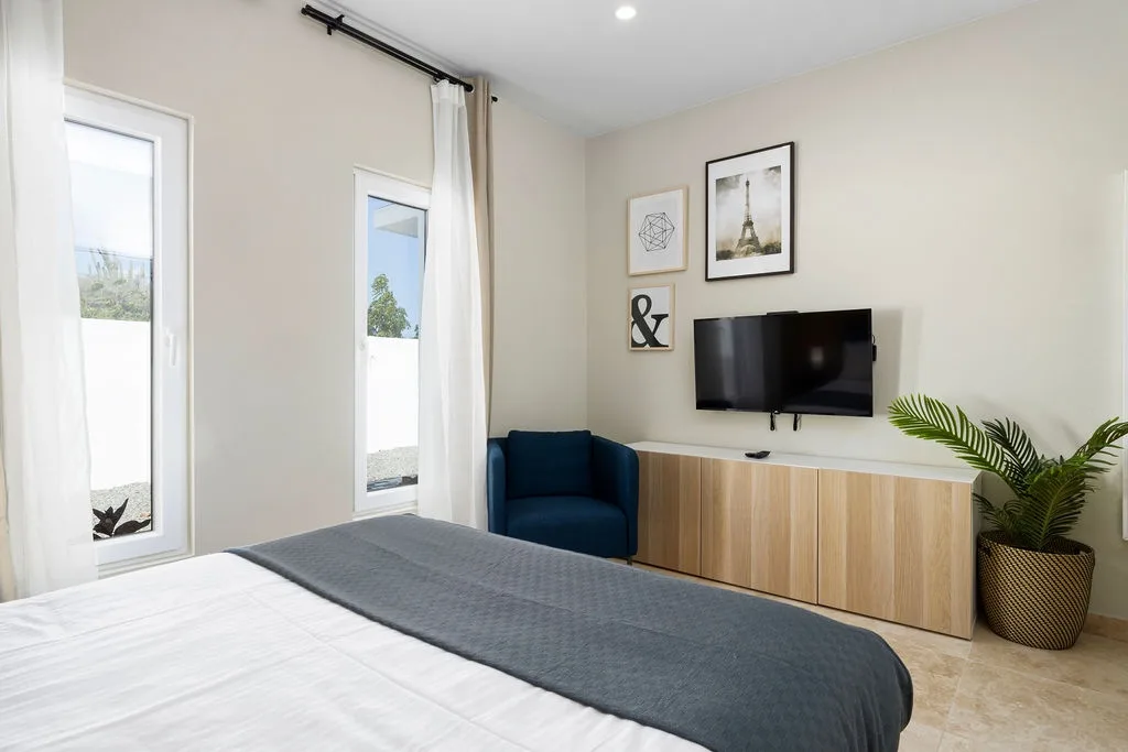 Unwind in your serene bedroom with modern touches, a cozy armchair, and entertainment at your fingertips—your peaceful retreat awaits.