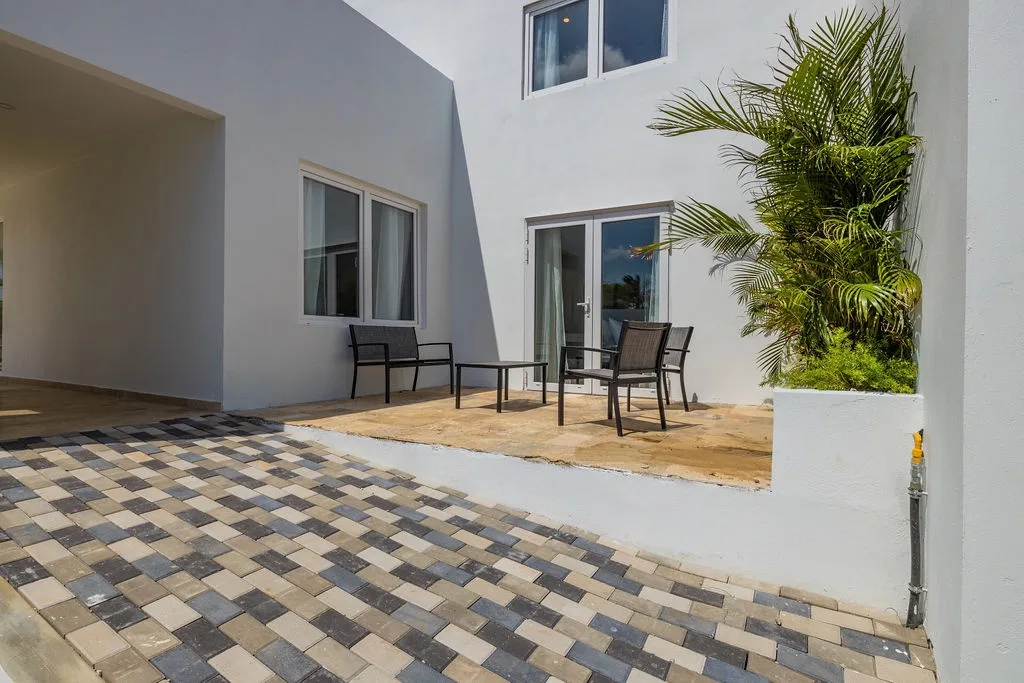 Modern white exterior with private patio featuring comfortable seating and lush tropical palms. Your peaceful outdoor retreat awaits with stylish paver flooring.