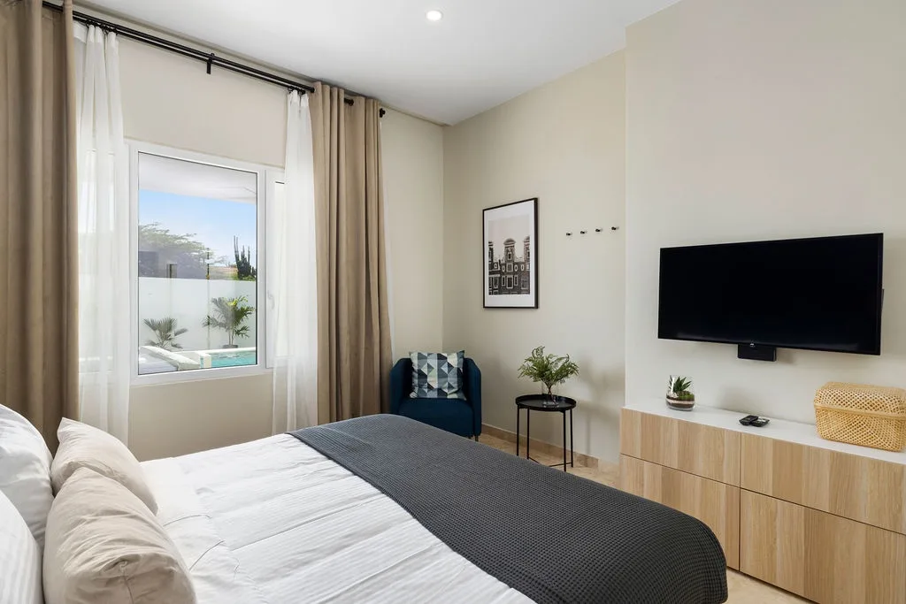Drift off in your serene bedroom with crisp linens, a cozy armchair, and soothing views of the pool through bright windows. Modern comforts meet calming design.