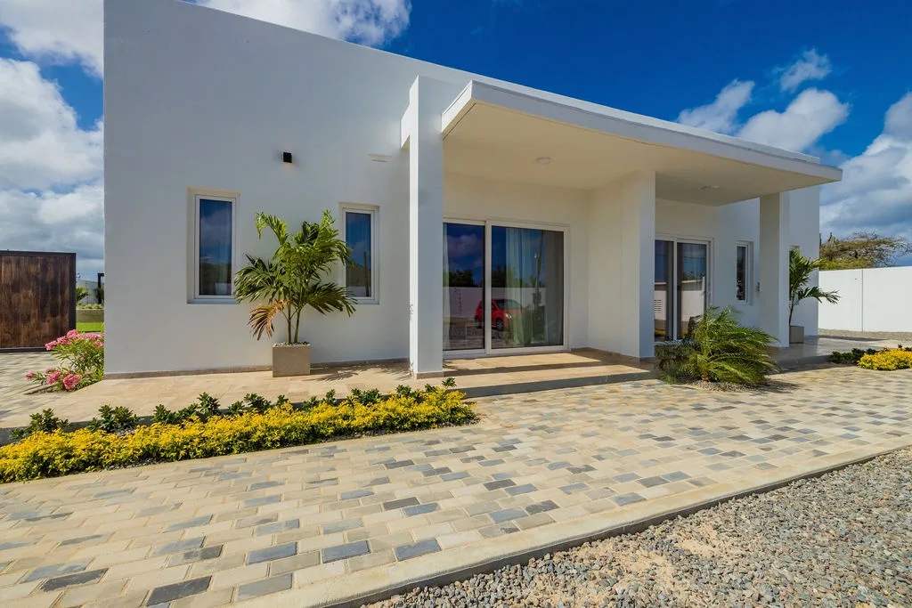 A striking modern property exterior framed by vibrant tropical landscaping and elegant paver driveway, inviting you to your tranquil island escape.