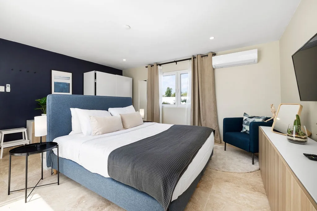 Drift off in this serene bedroom featuring a plush bed with crisp linens and a cozy accent chair perfect for unwinding. Fresh air and natural light pour through the window, while climate control keeps your stay comfortable year-round.