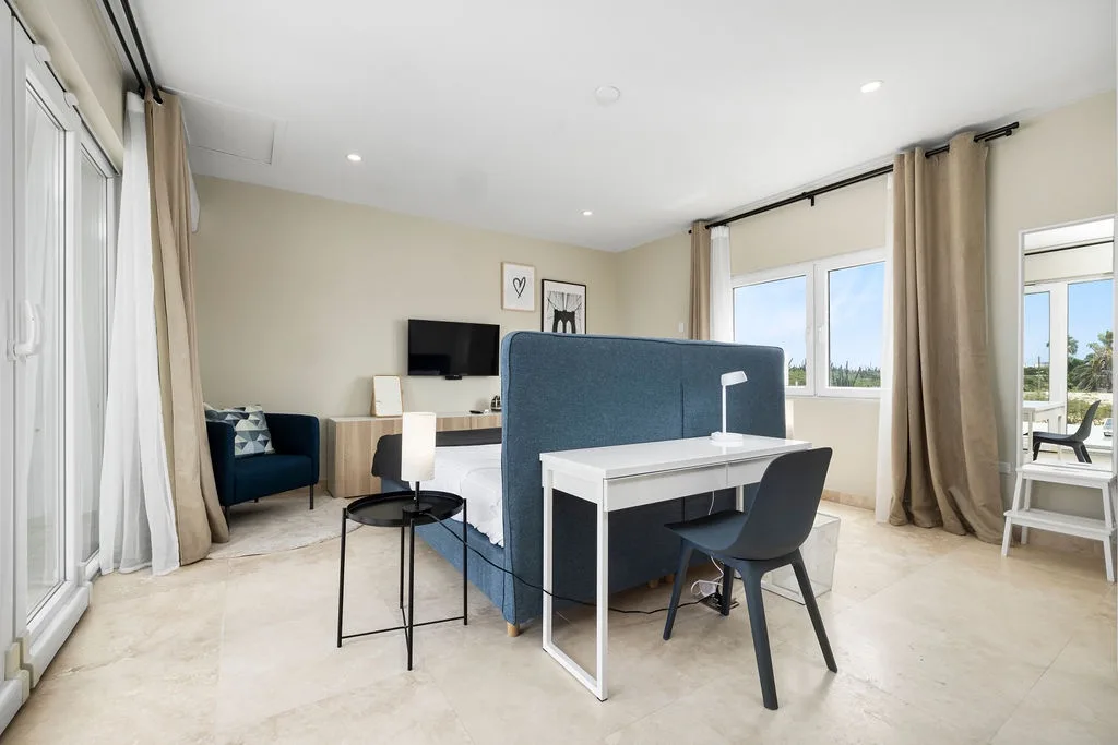 Step into your bright and comfortable bedroom suite, where soft neutral tones, modern furnishings, and a private workspace create the perfect retreat. Natural light floods through large windows framing peaceful outdoor views.