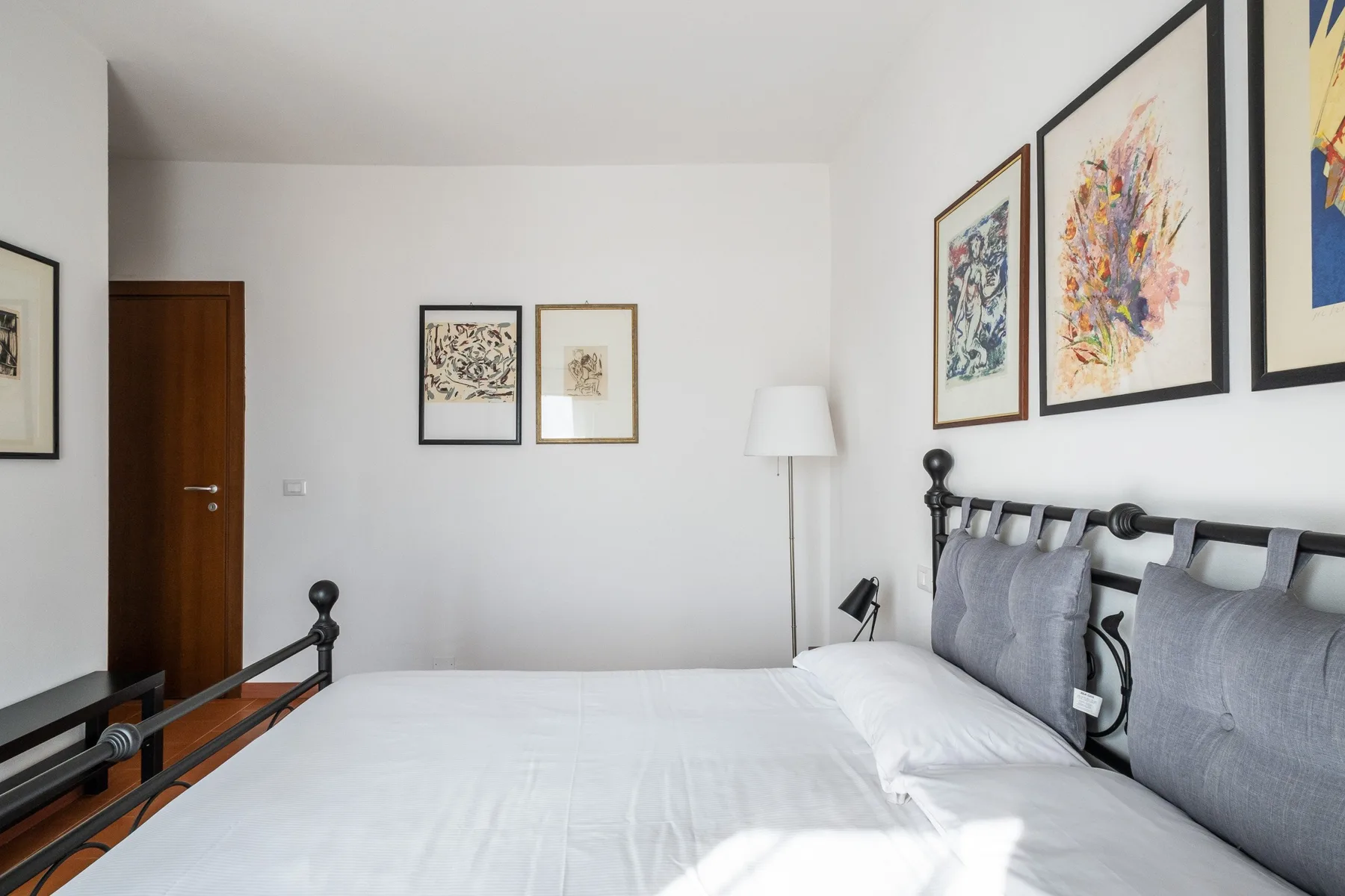 A bright bedroom with a neatly made bed and framed artwork on the walls.