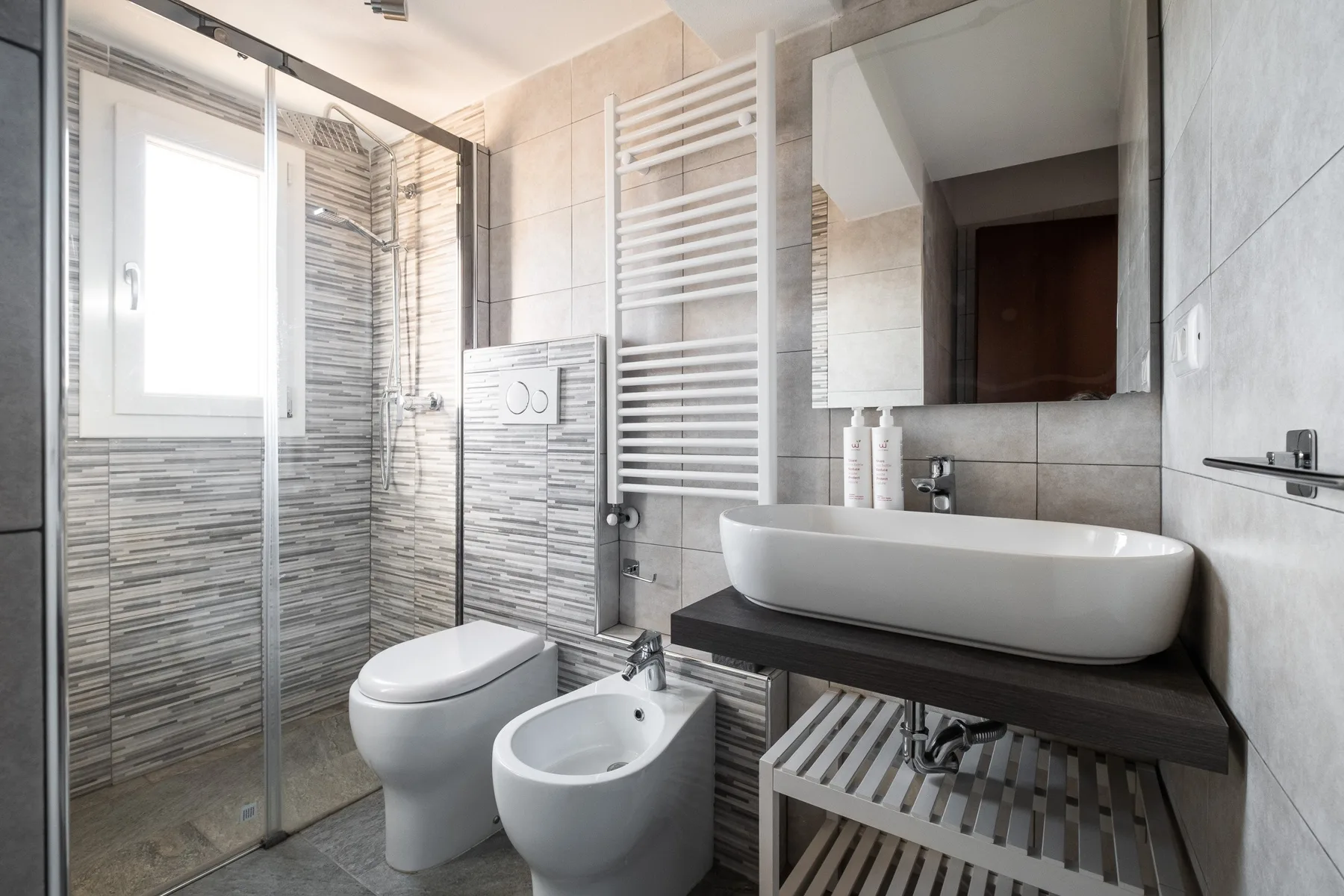 A tiled bathroom with a glass shower, bathtub, toilet, and sink.