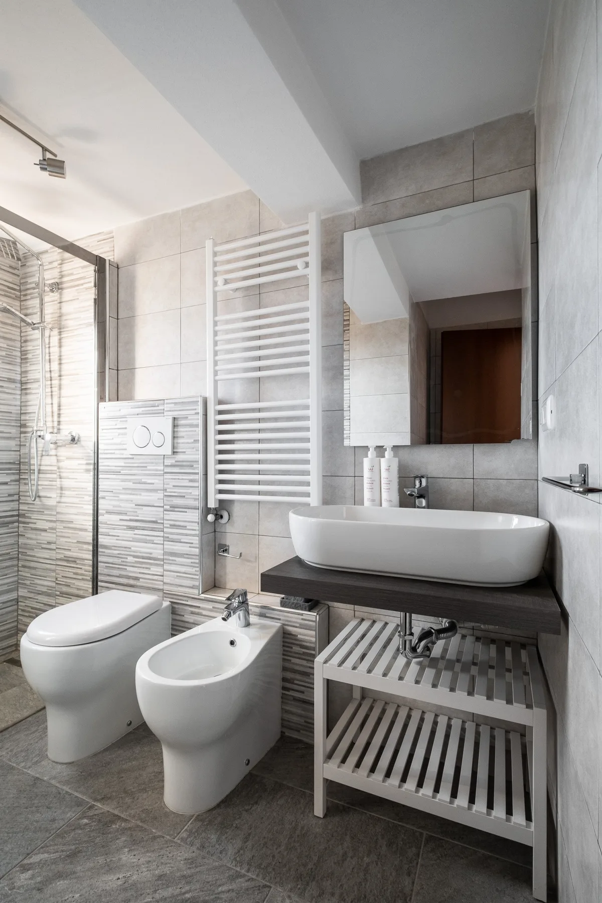 A tiled bathroom with a sink, mirror, toilet, and bidet.