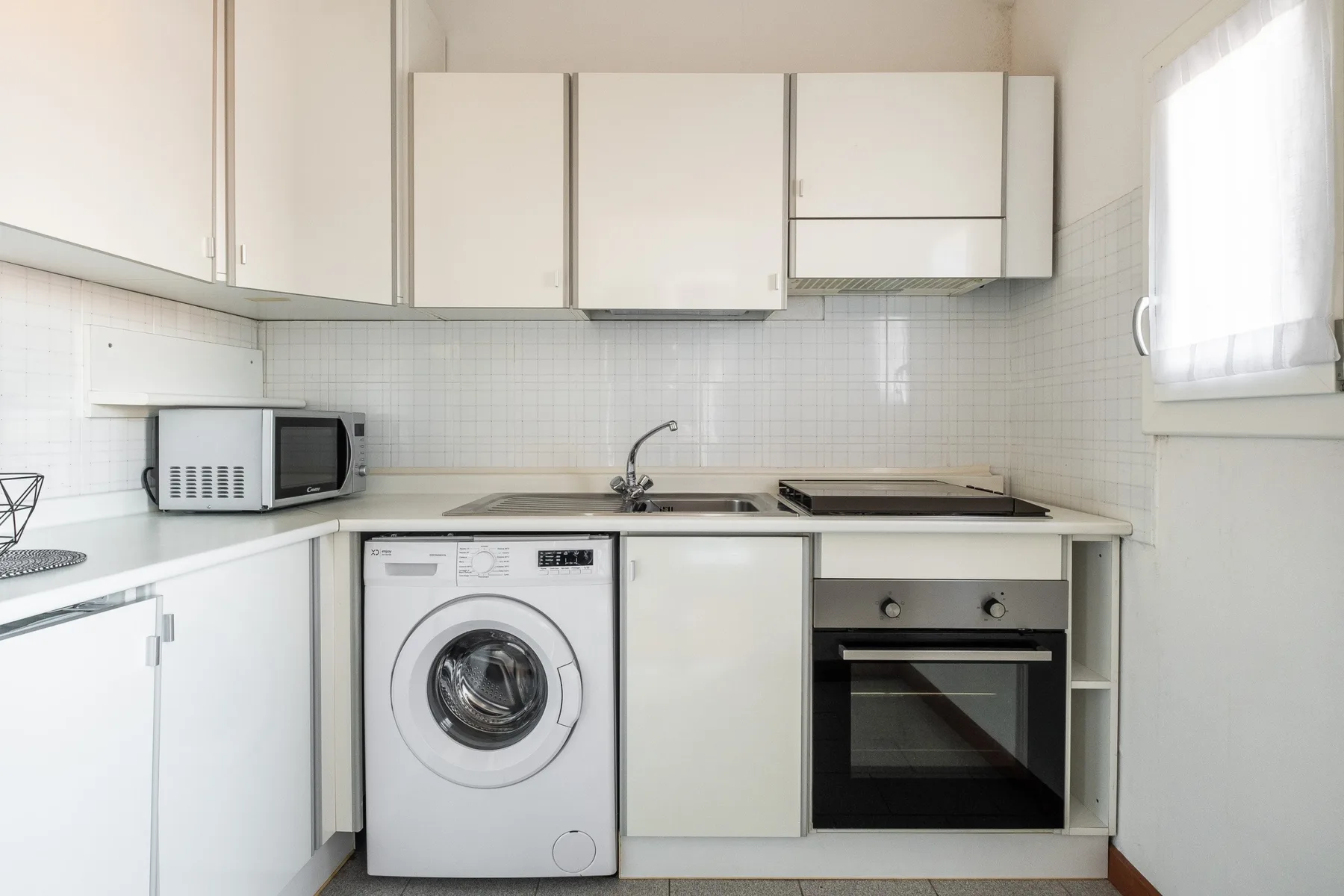 A bright kitchen with white cabinets, a washing machine, and an oven.