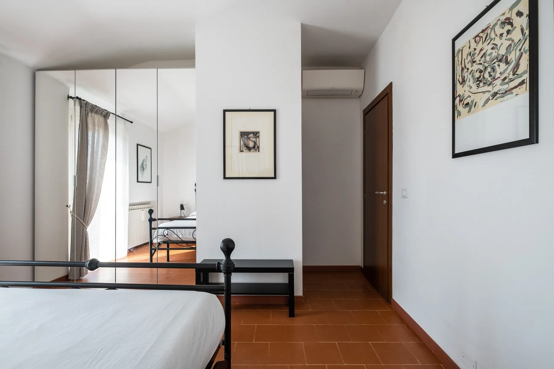 A bedroom with a bed, framed artwork, and a wooden door.