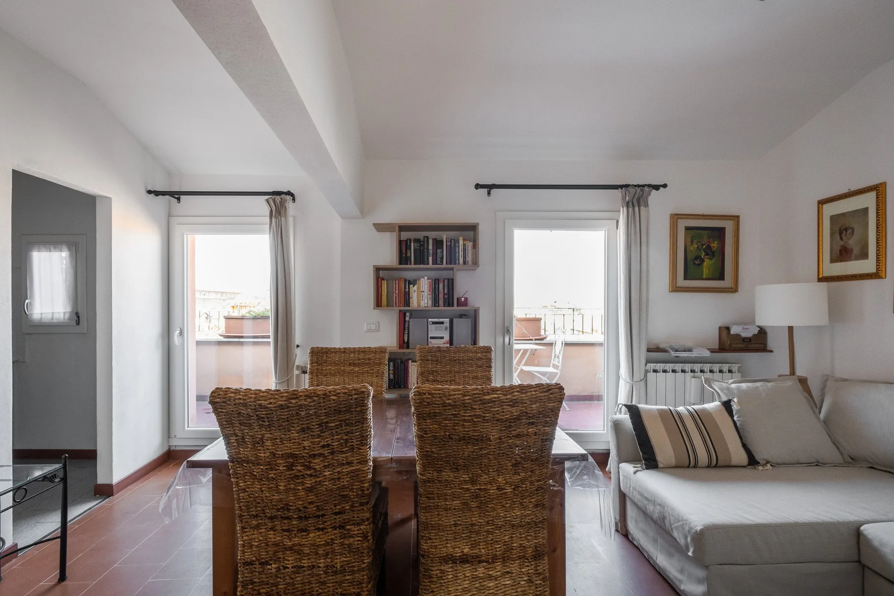 Una luminosa sala de estar y comedor con mesa, asientos de mimbre y sofá.