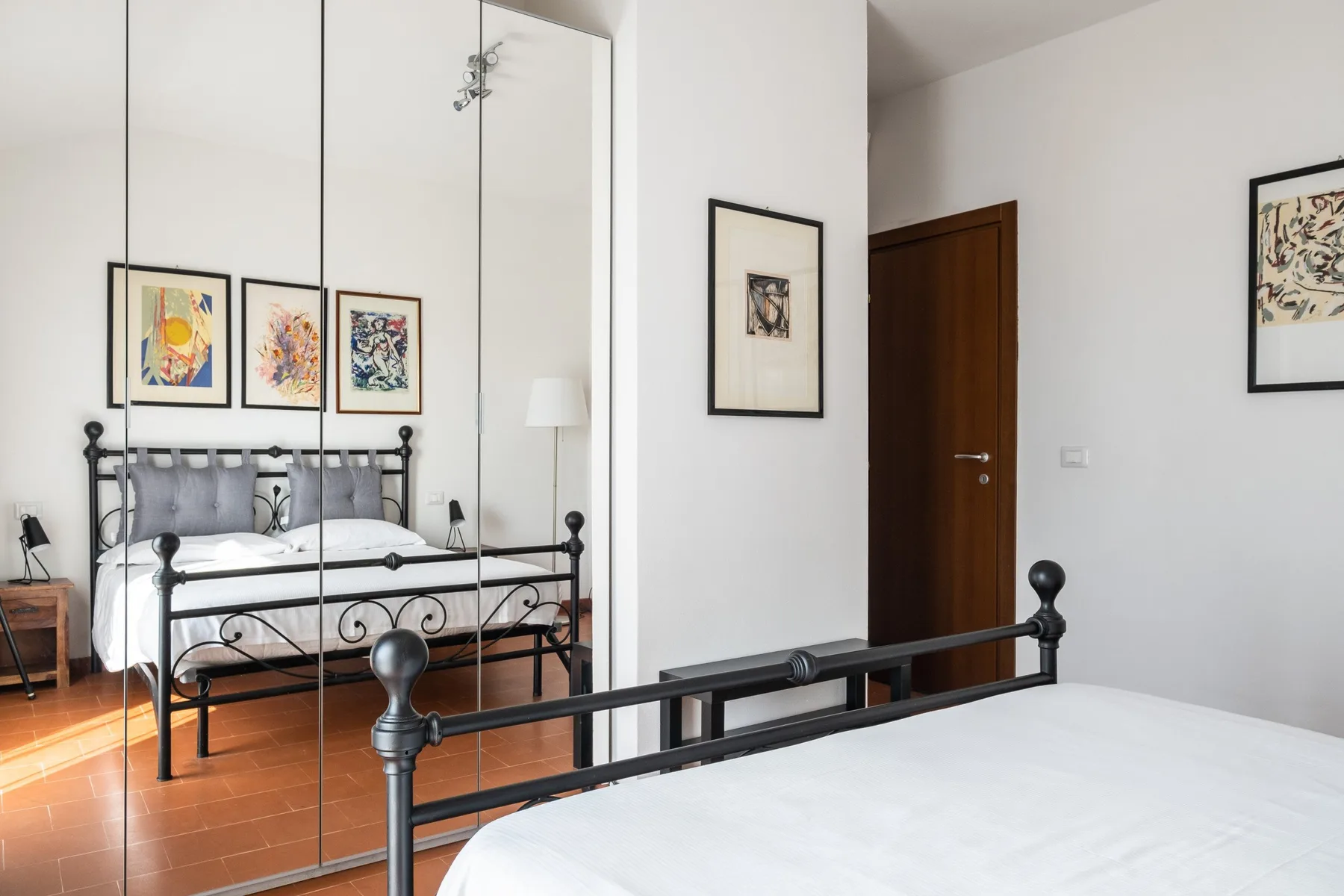 A bedroom with black metal beds, framed artwork, and a wooden door.