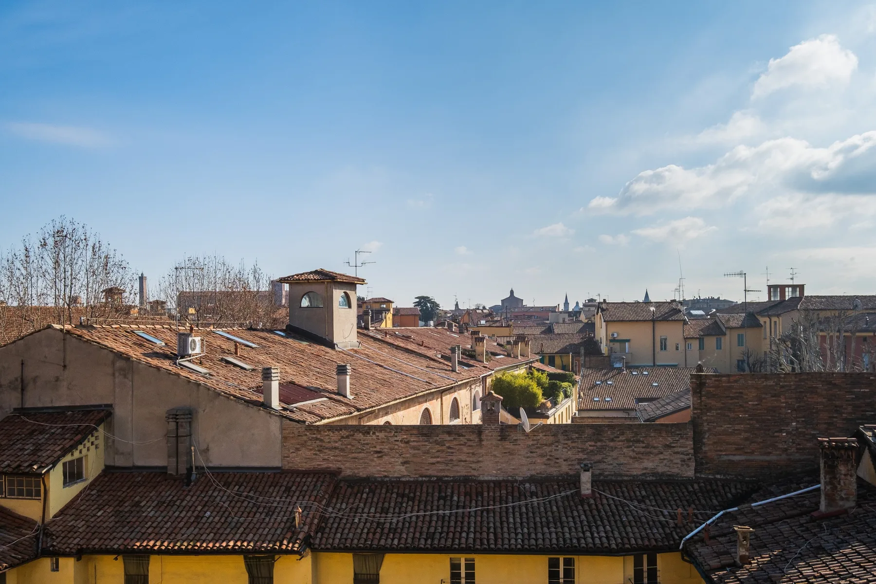 A cityscape of tiled rooftops and buildings beneath a blue sky.
