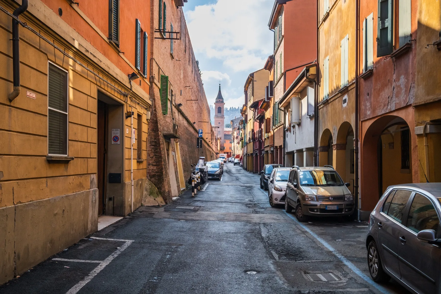 A narrow street runs between rows of colorful buildings, with parked cars along the sides.