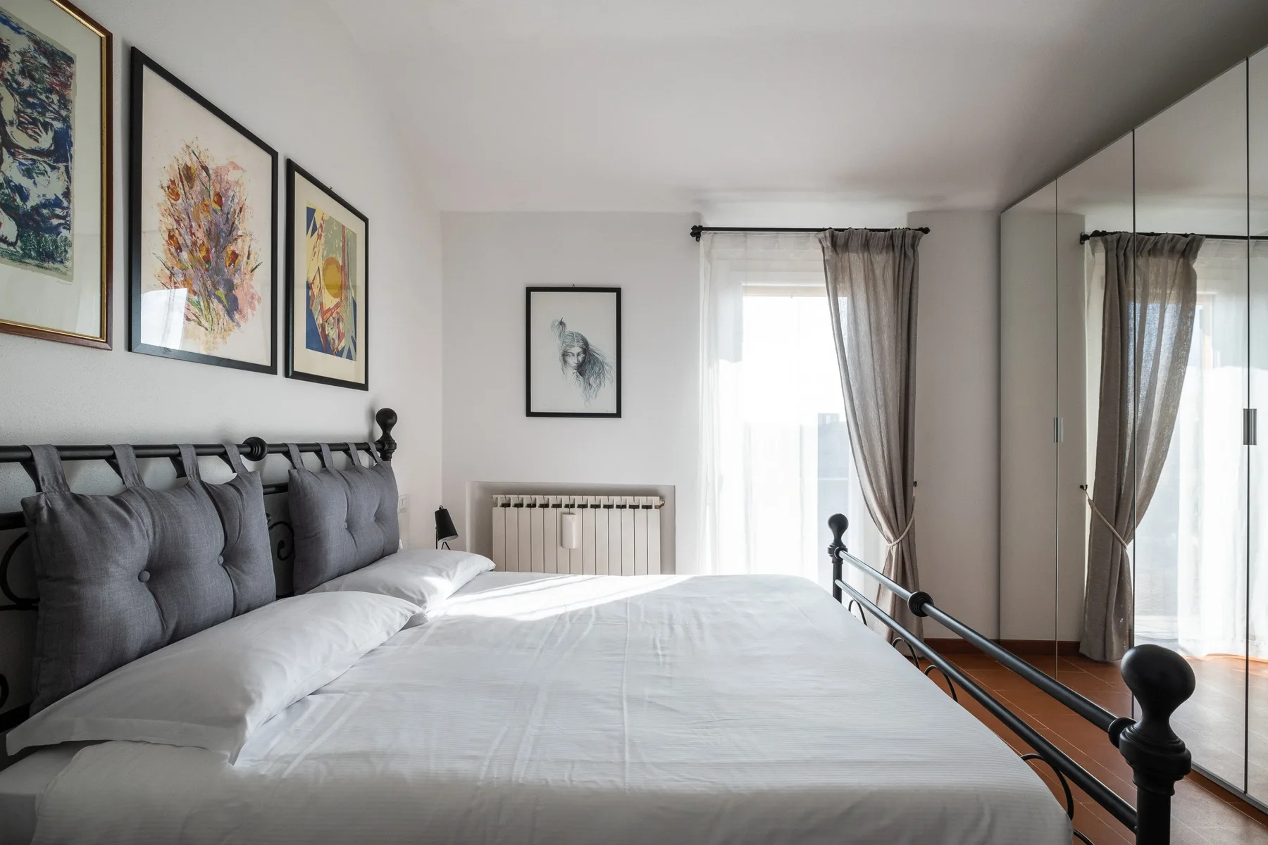 A bedroom with a large bed, framed artwork, and a curtained window.