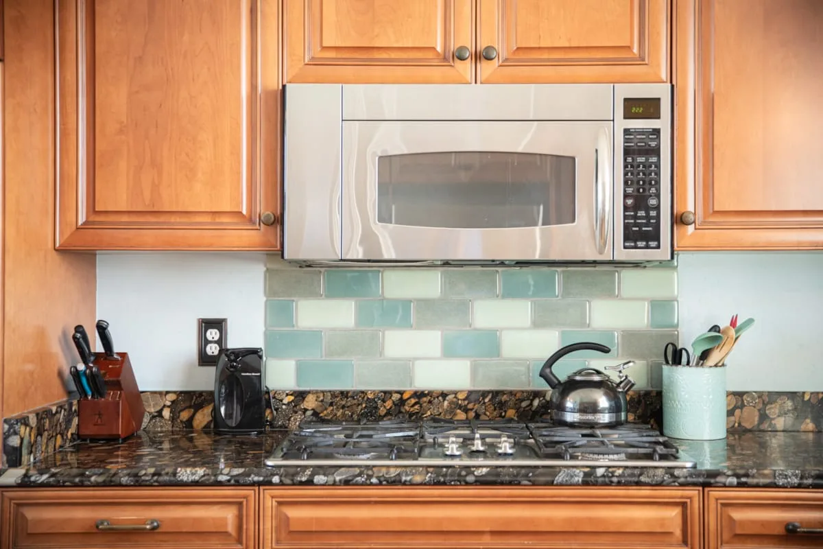 Una estufa de cocina está debajo de un microondas, con gabinetes de madera y un salpicadero de azulejos.