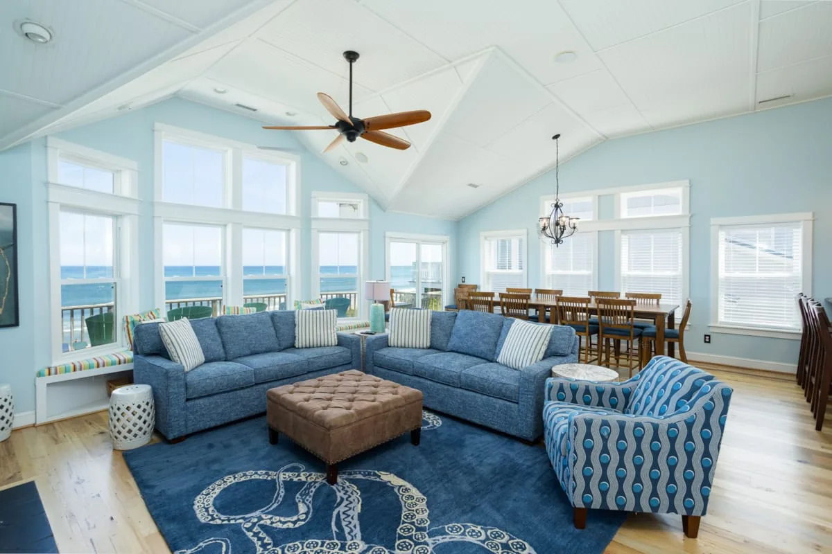 A bright living room with blue seating and large windows overlooking the water.