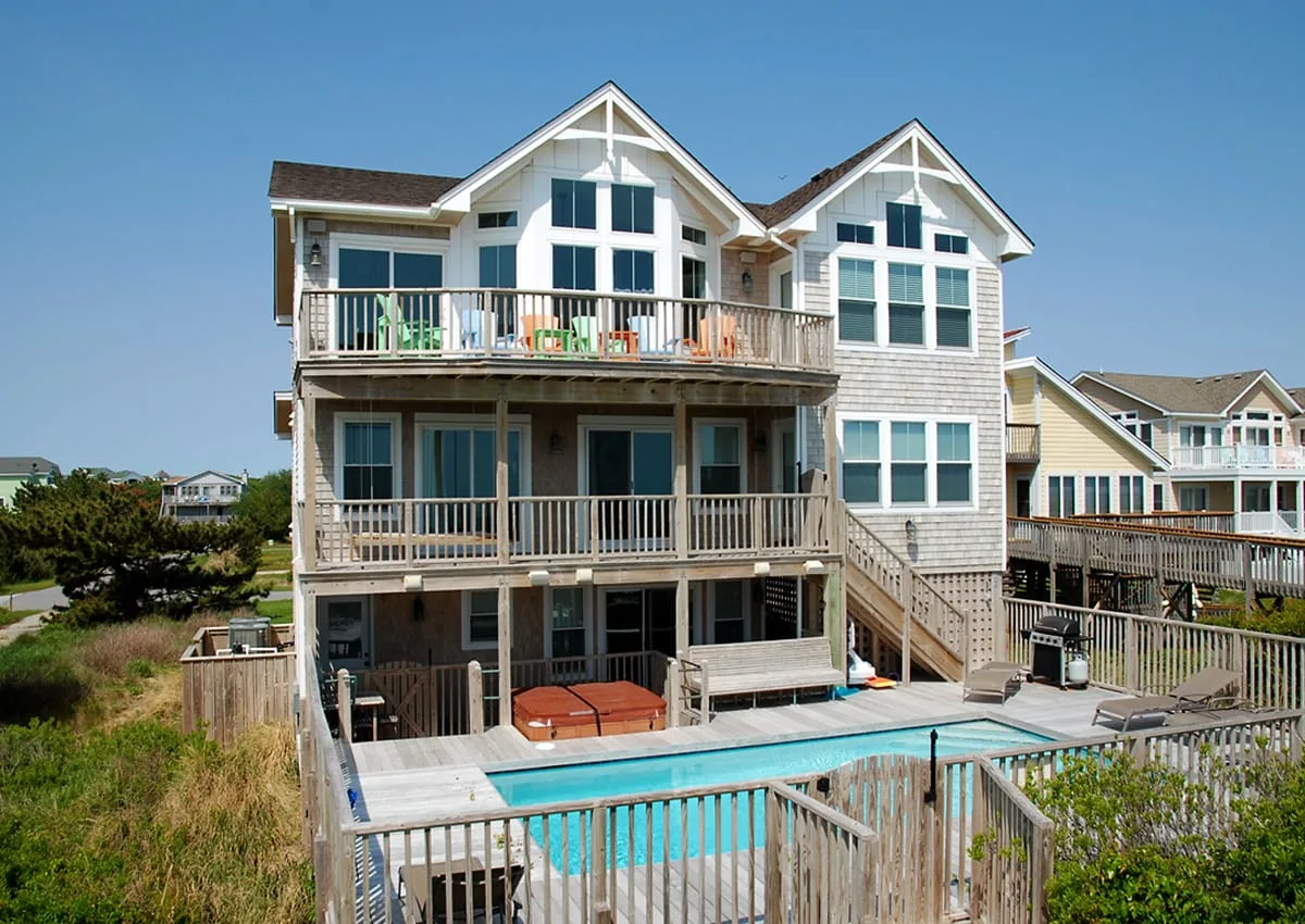 Una casa grande con balcones da a una piscina cercada.