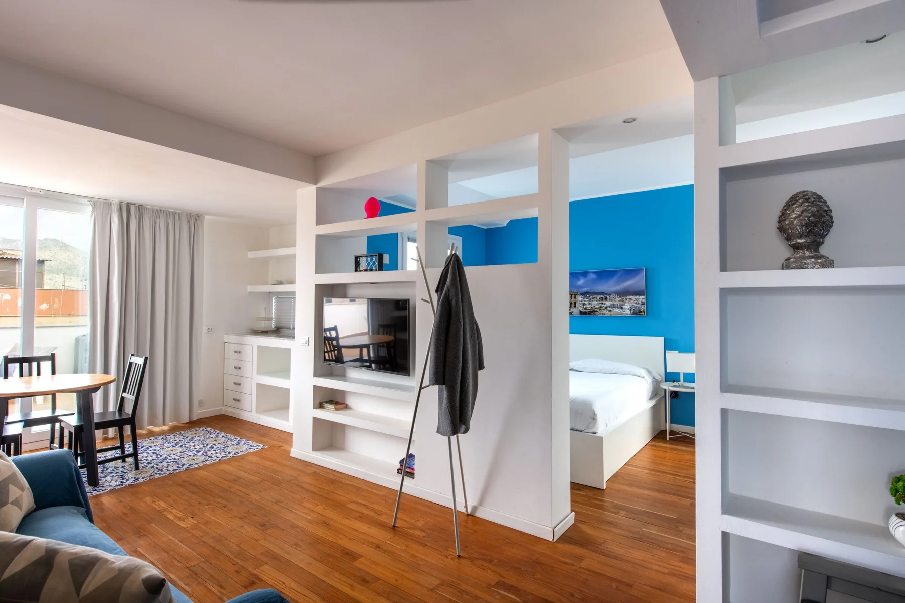 A bright open-plan room combines a dining area, living space, and bedroom with blue walls.