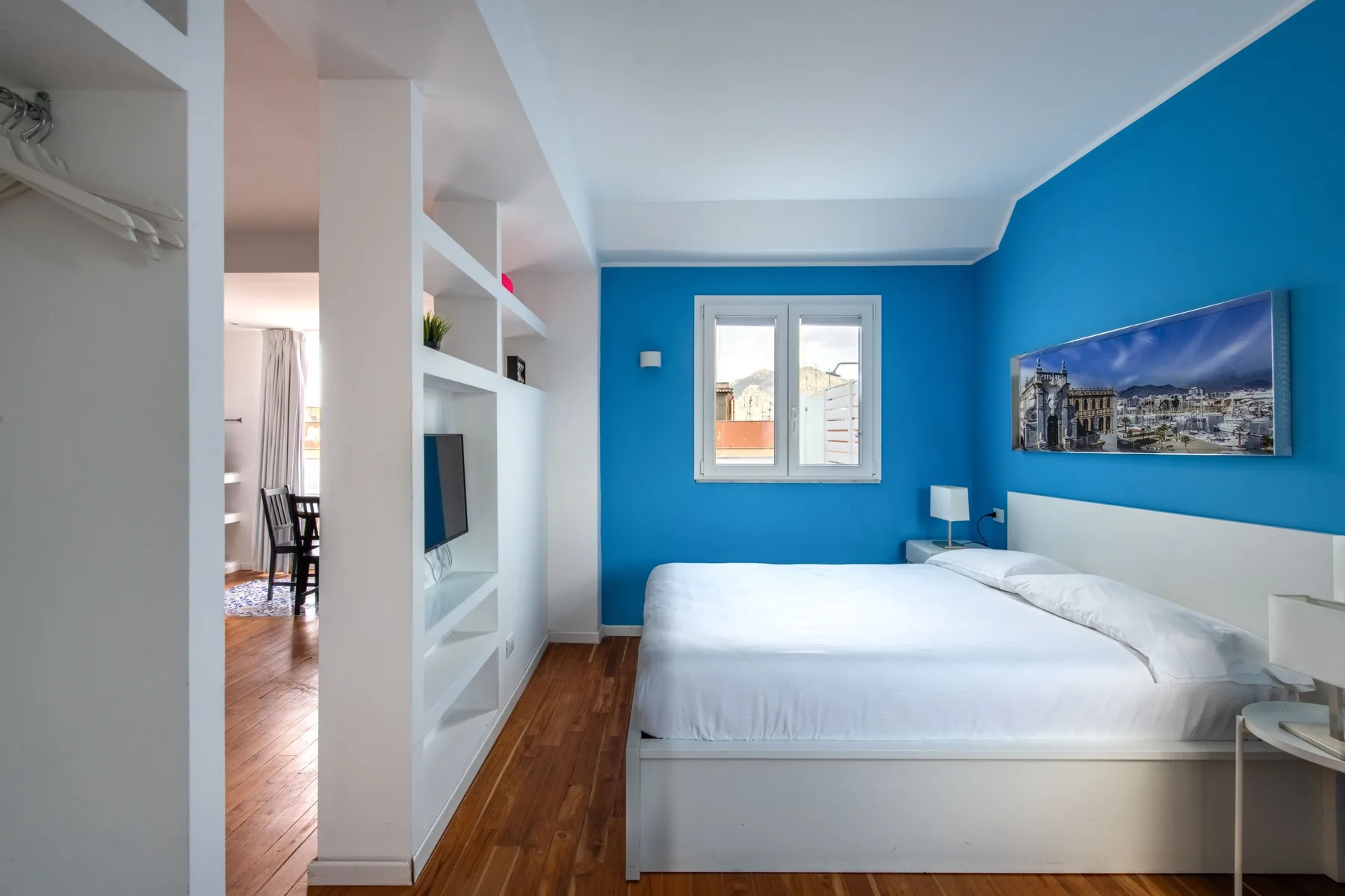 A bedroom with a bed, blue walls, and a built-in shelving unit.
