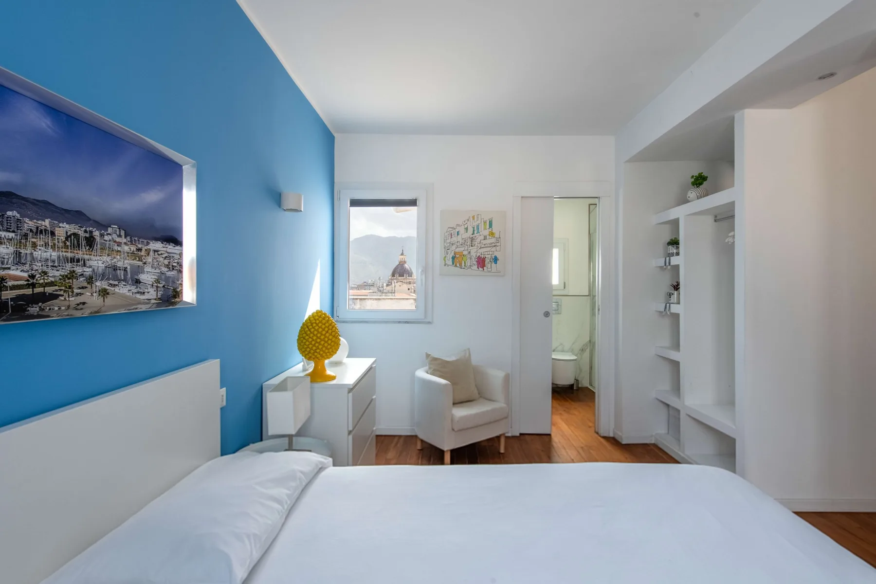 A bright bedroom with a bed, a small seating area, and built-in shelving.