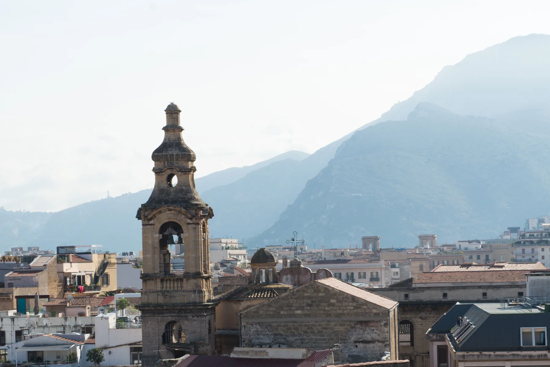 City rooftops and a bell tower sit before a mountain backdrop.