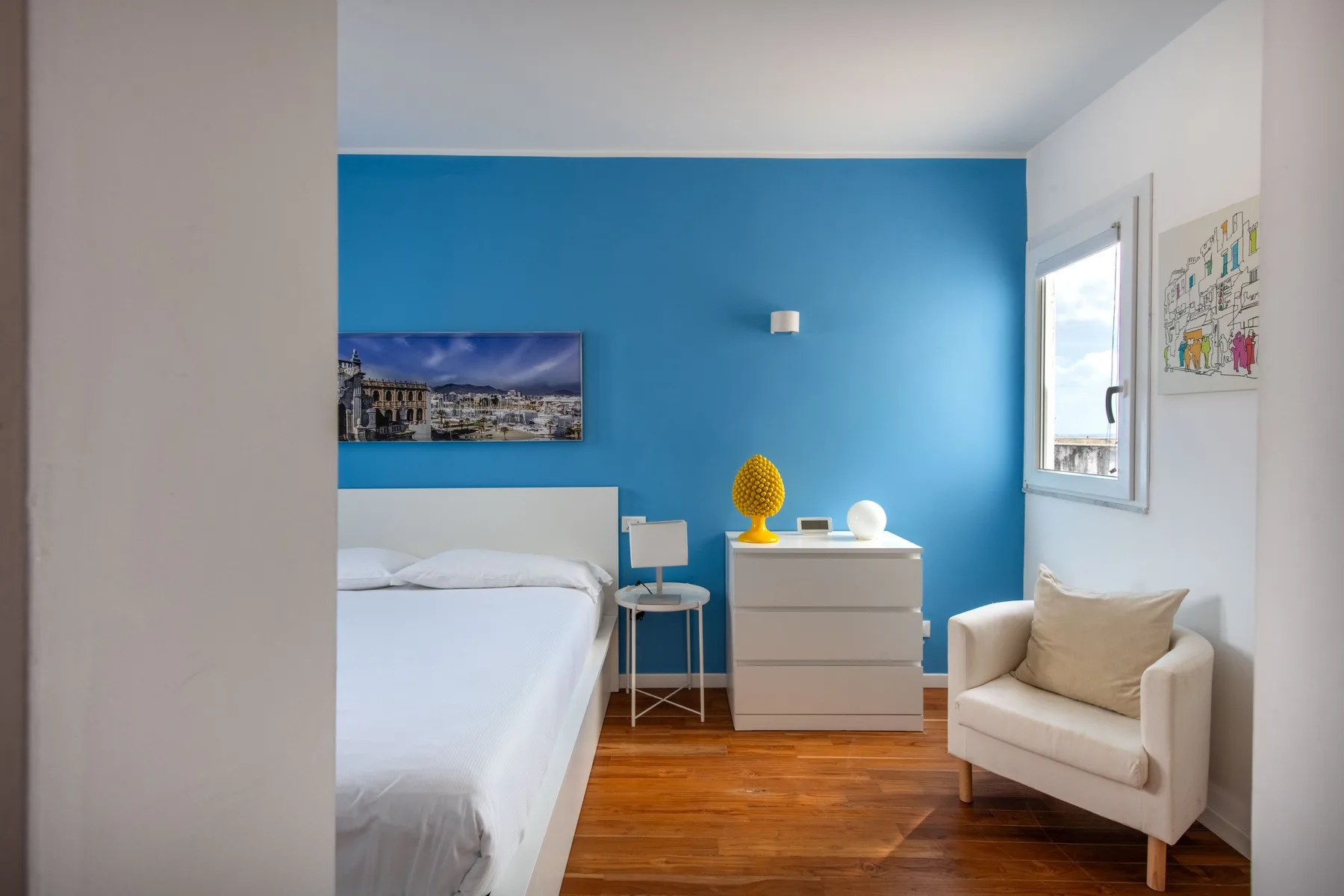 A bright bedroom with a bed, a blue accent wall, and a cushioned seat.