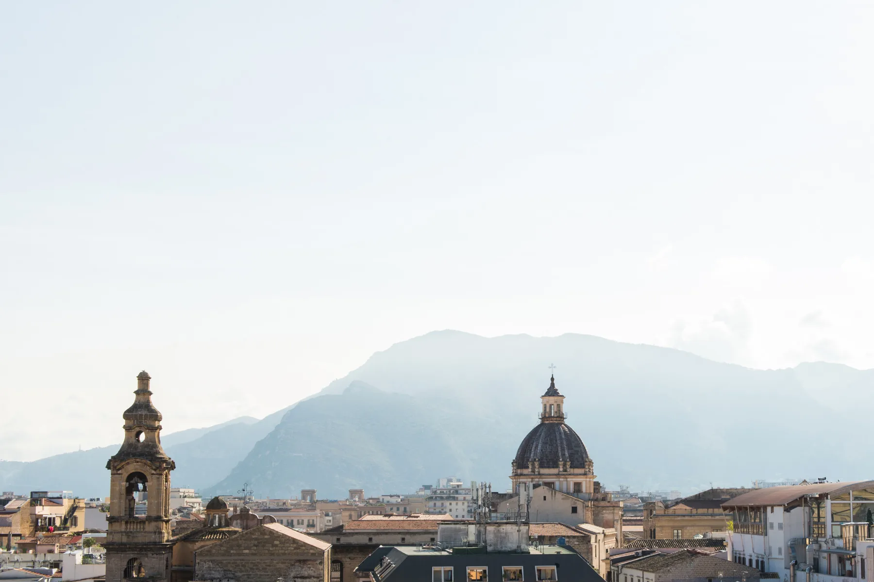 A city skyline with historic domed buildings and mountains in the background.
