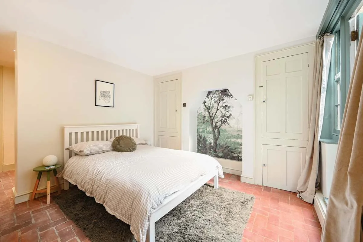 Un dormitorio con una cama blanca, una alfombra estampada y ventanas altas.