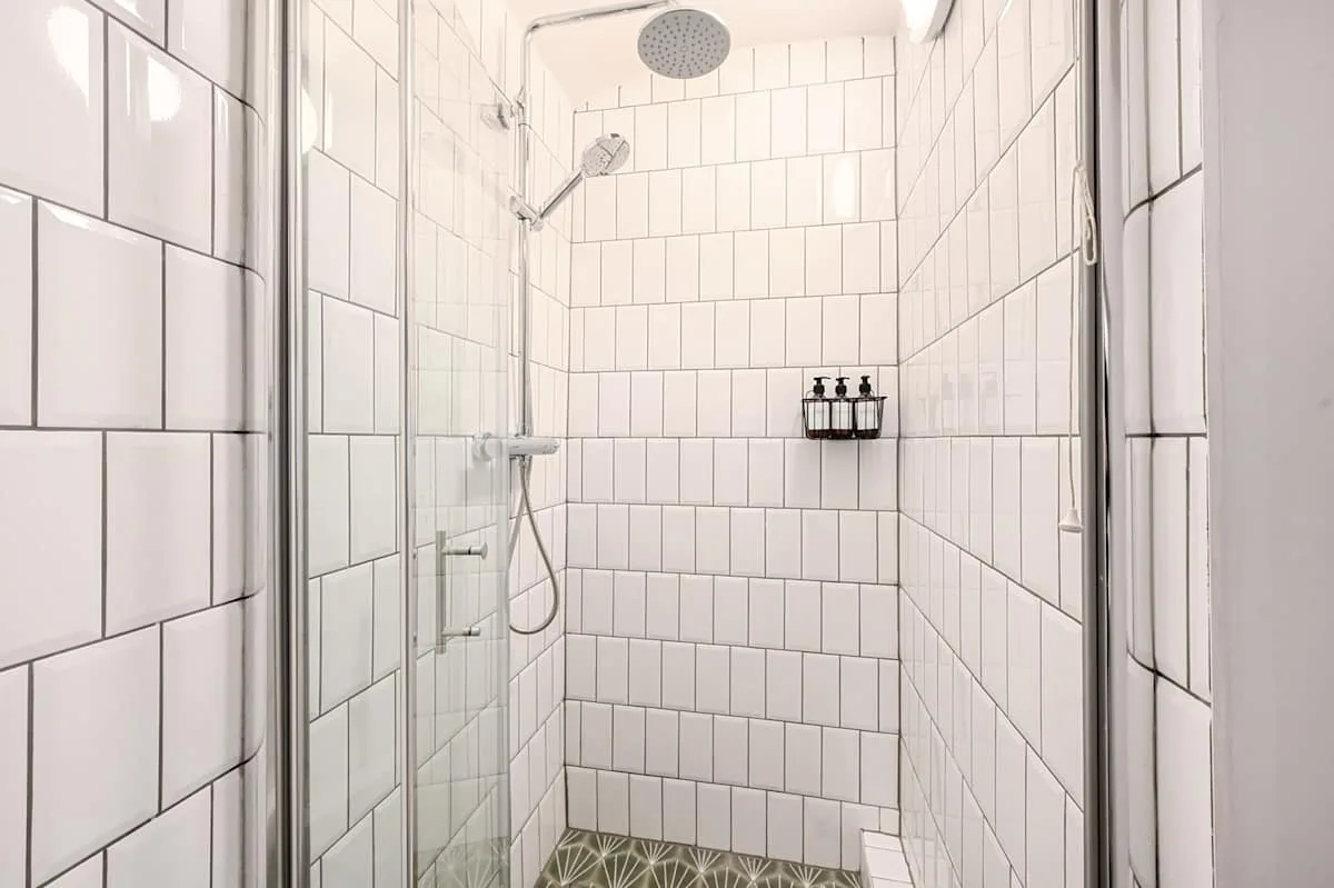 Una ducha con azulejos, cabezales de ducha en la pared y una pequeña repisa para jabón.