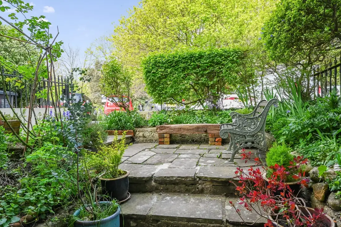 A leafy garden patio with stone steps, planted borders, and outdoor seating.
