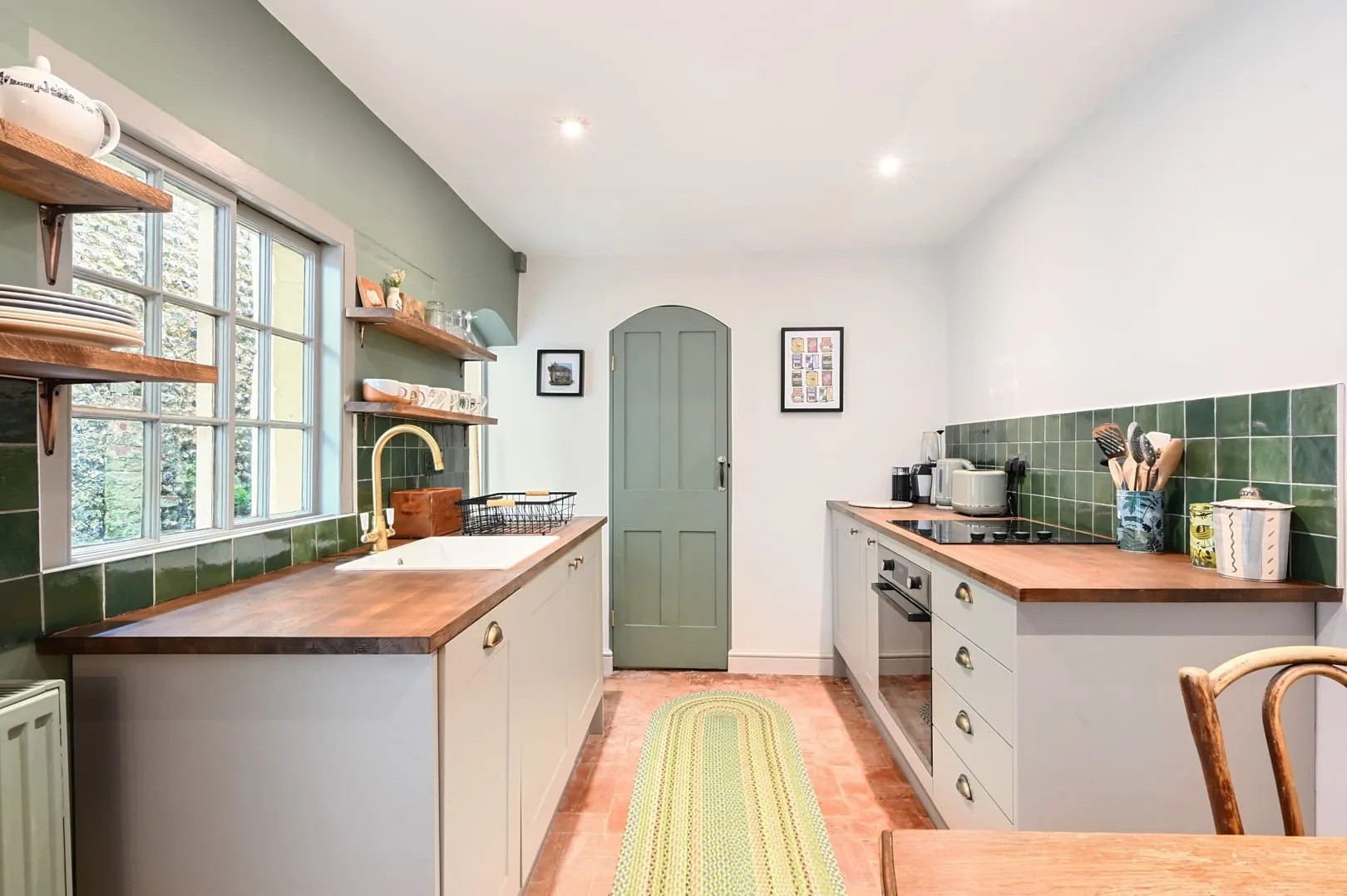 Una cocina alargada con encimeras de madera y salpicaderos de azulejos verdes.