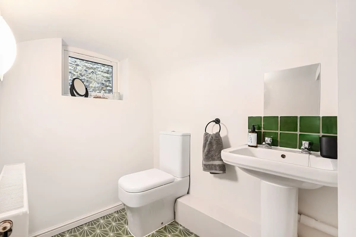 Un baño luminoso con inodoro, lavabo con pedestal y azulejos verdes.