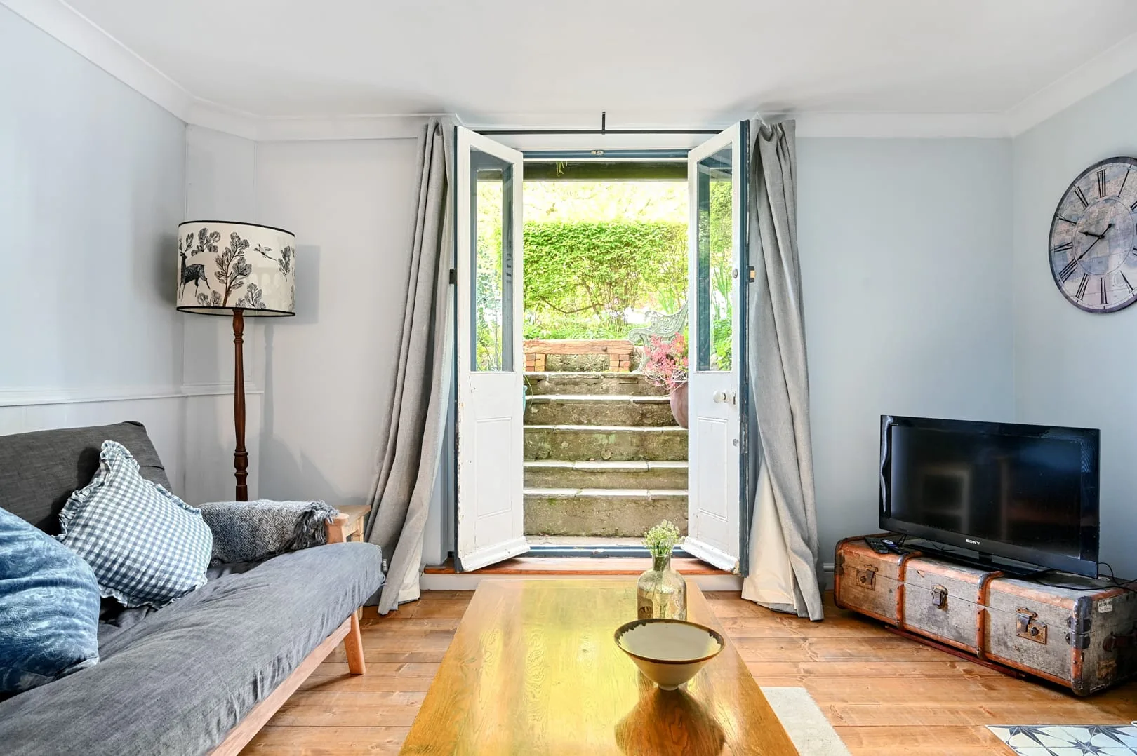 A living room with seating, a coffee table, and open doors to a garden.