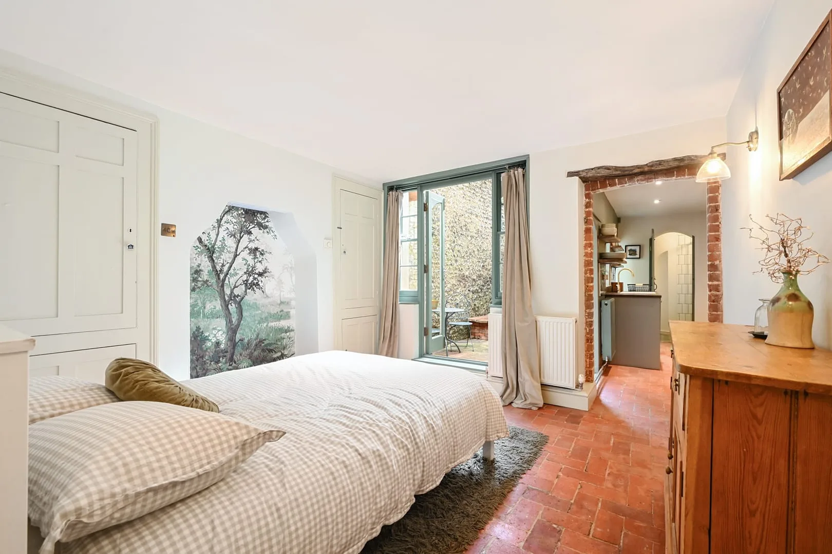 A bedroom with a bed, sliding glass doors, and a view into a small kitchen.