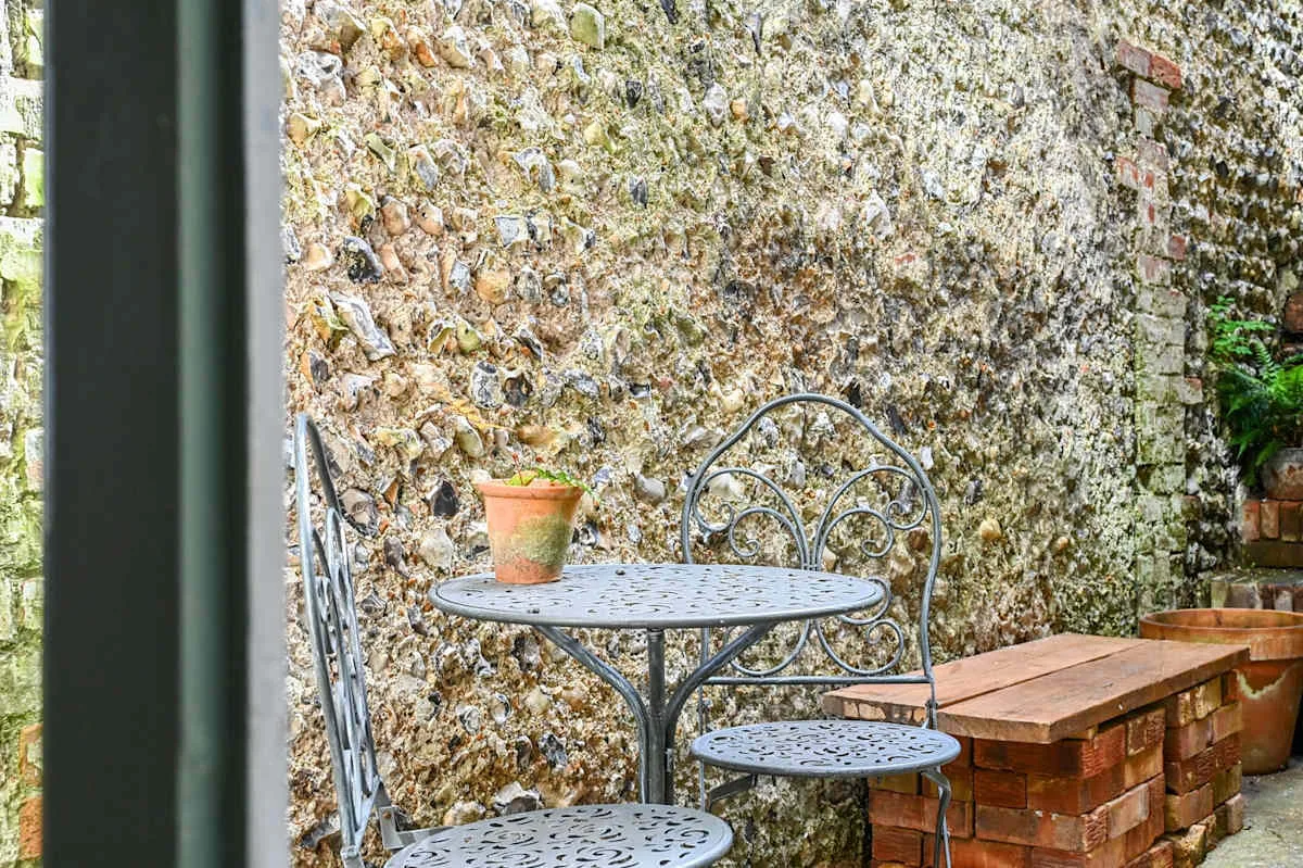 Una zona de estar al aire libre con una mesa metálica redonda junto a un muro de piedra.