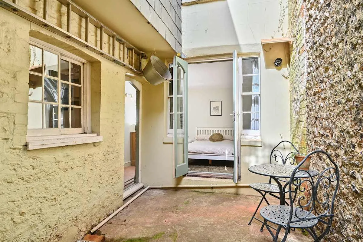 Un pequeño patio con una mesa y asientos metálicos junto a la entrada de un dormitorio.