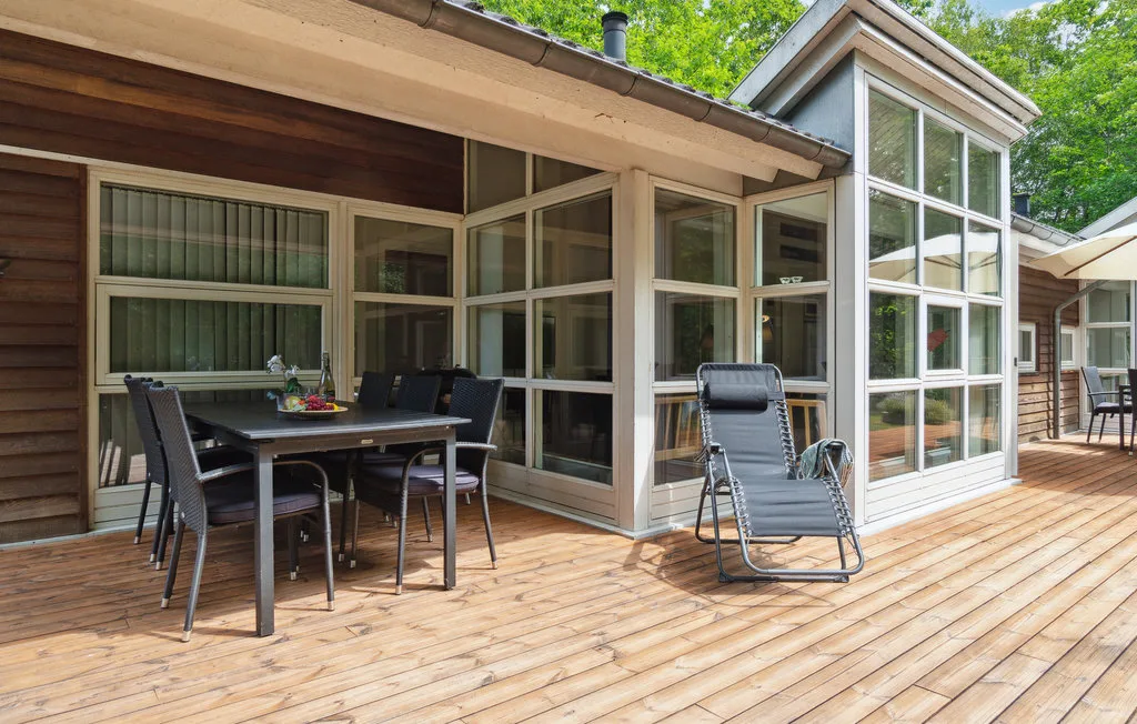 Una terraza de madera junto a una casa tiene una mesa de comedor y asientos de descanso.