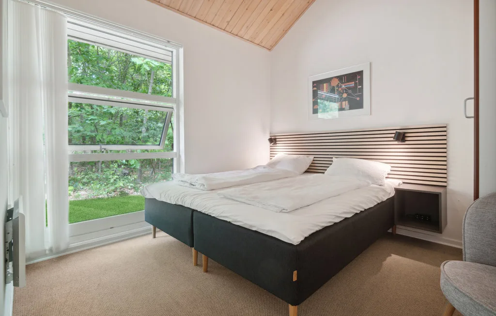 Un dormitorio luminoso con una cama grande junto a una ventana con vistas a la vegetación.