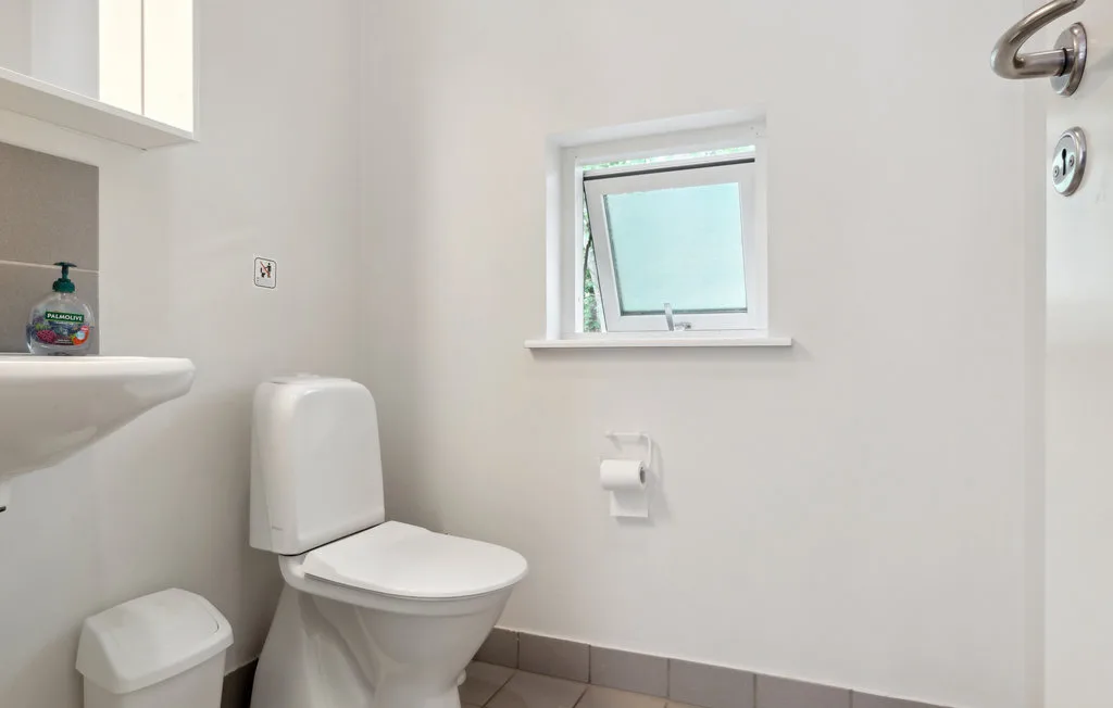 Un baño luminoso con inodoro, lavabo y una ventana pequeña.