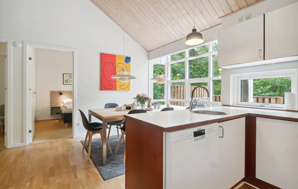 Una cocina luminosa con una isla central y un comedor junto a grandes ventanas.