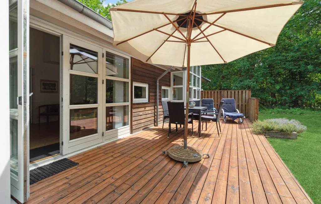 Una terraza de madera junto a la casa tiene asientos al aire libre bajo una sombrilla grande.