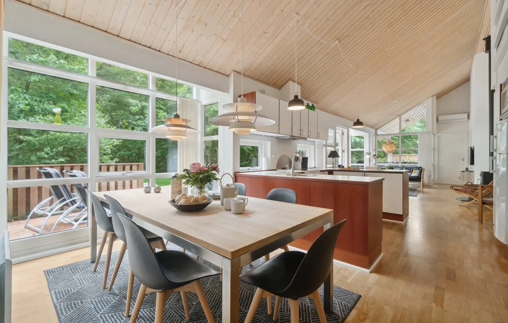 Una luminosa cocina-comedor de planta abierta con grandes ventanas y una mesa de madera.