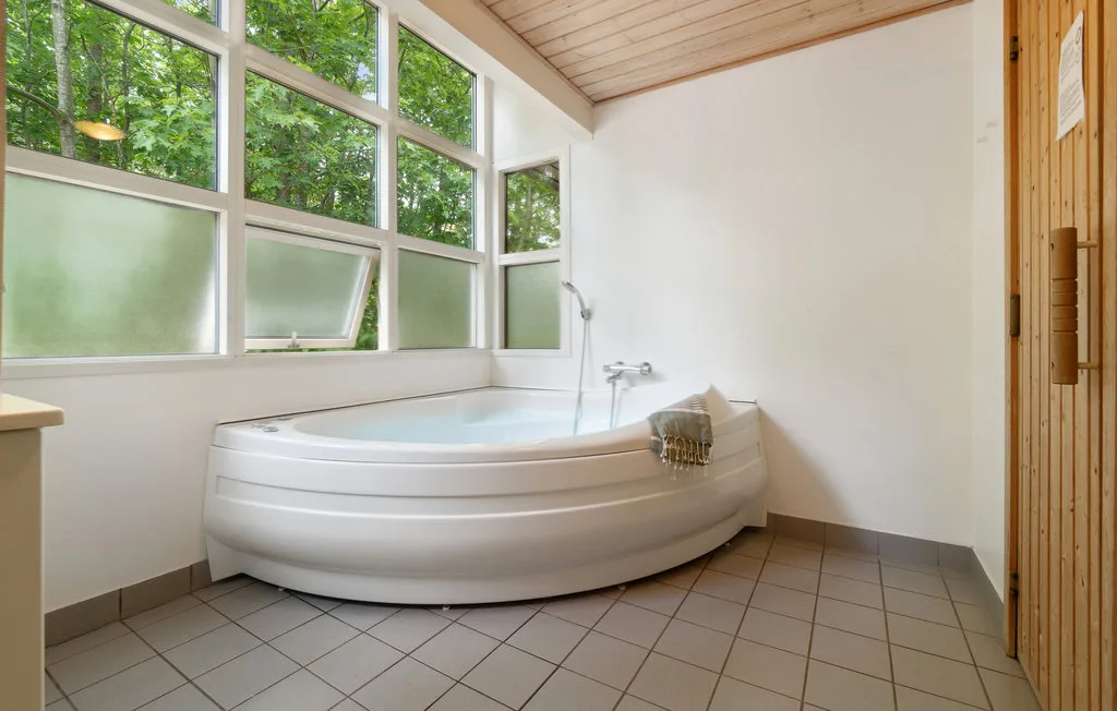 Un baño con una amplia bañera de esquina debajo de grandes ventanas.