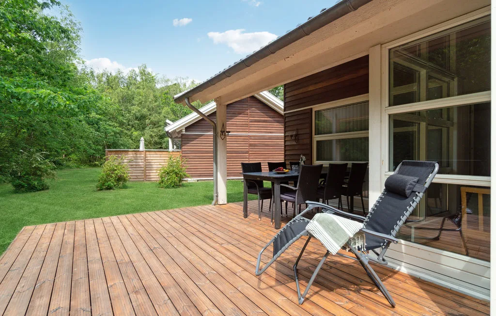 Una terraza de madera junto a una casa tiene asientos y una mesa.