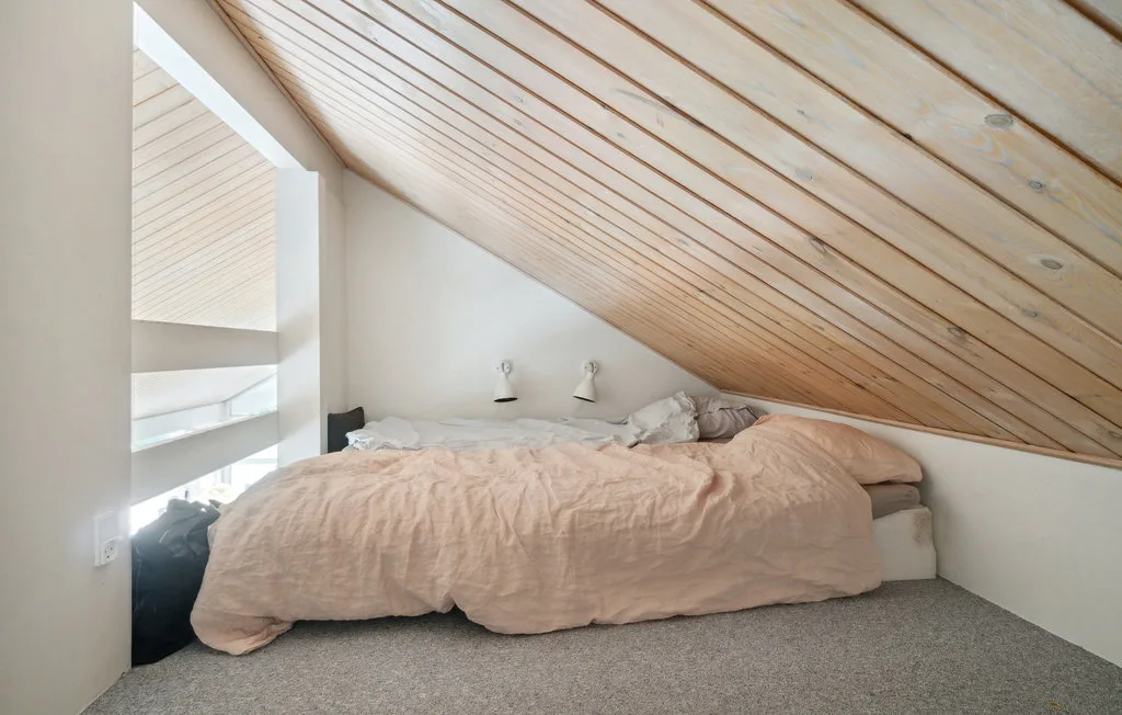 Un dormitorio con una cama bajo un techo inclinado de madera.
