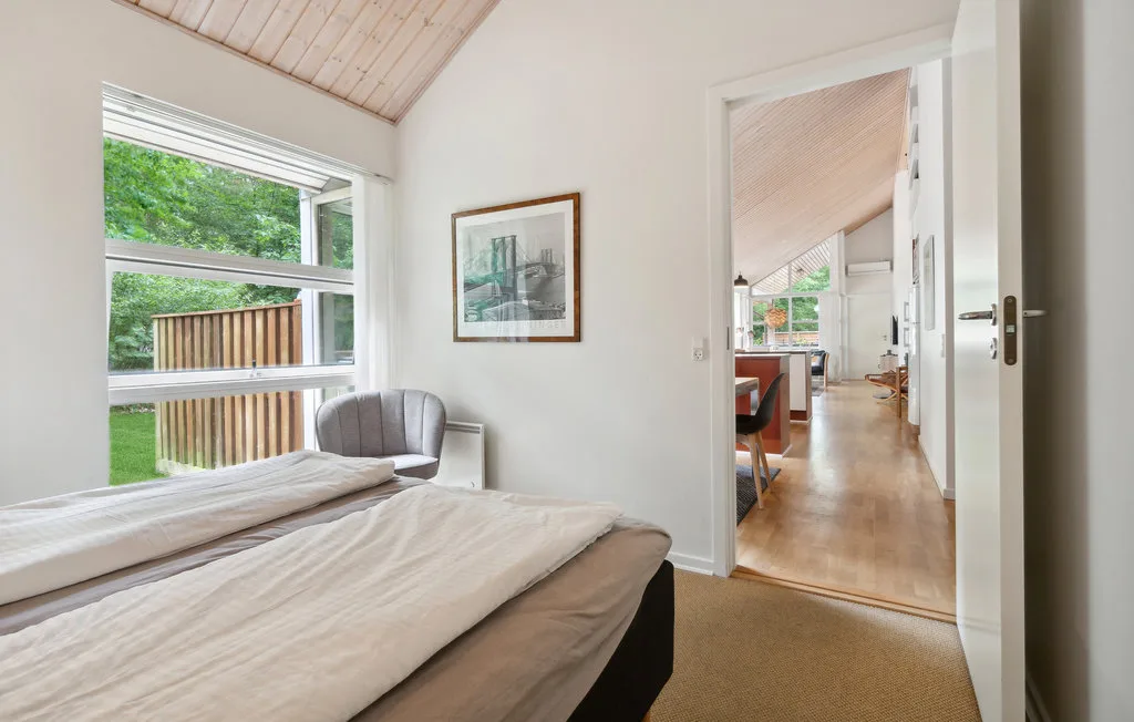 Un dormitorio con una cama junto a una ventana amplia con vistas a la vegetación.