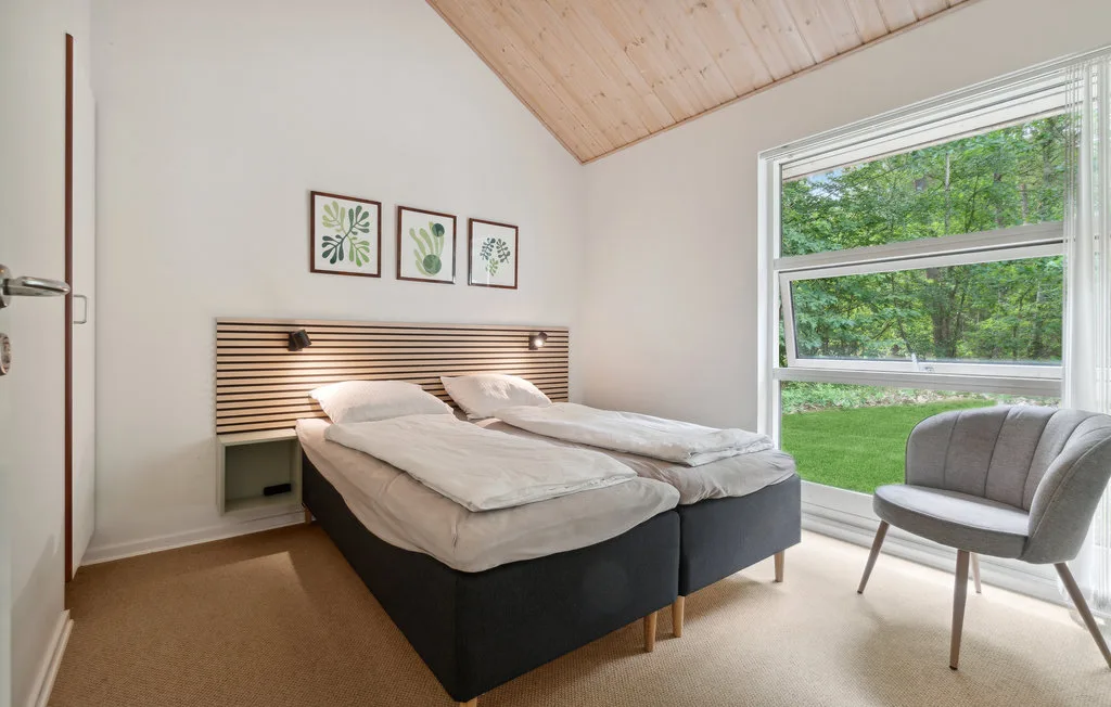 Un dormitorio con dos camas junto a una gran ventana con vistas a la vegetación.