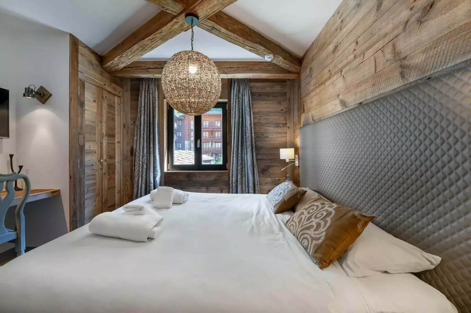 Un dormitorio con una cama grande bajo vigas de madera vistas y una lámpara colgante tejida.
